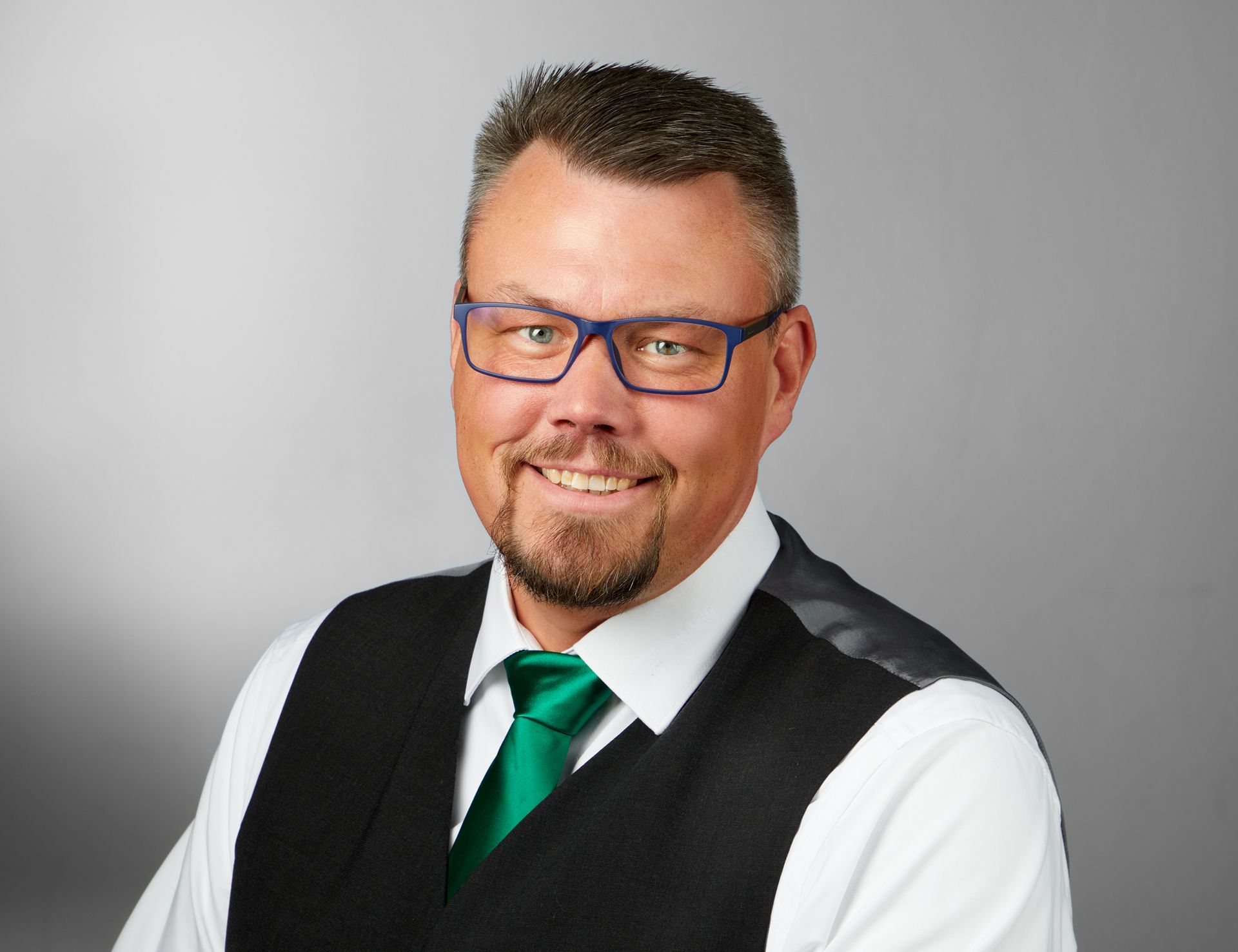 Ein Mann mit Brille und grüner Krawatte lächelt in die Kamera.