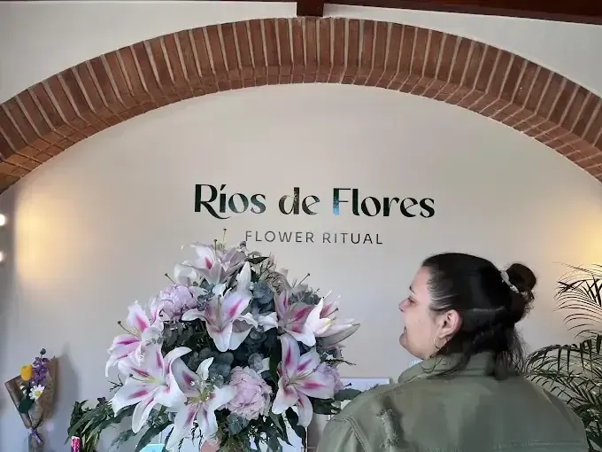 Una mujer admira un gran arreglo floral debajo del letrero de una tienda que dice 