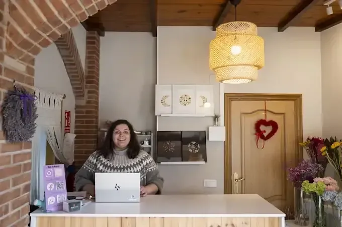 Mujer sonriendo en el mostrador de una floristería, con una laptop. Se ven un arco de ladrillo