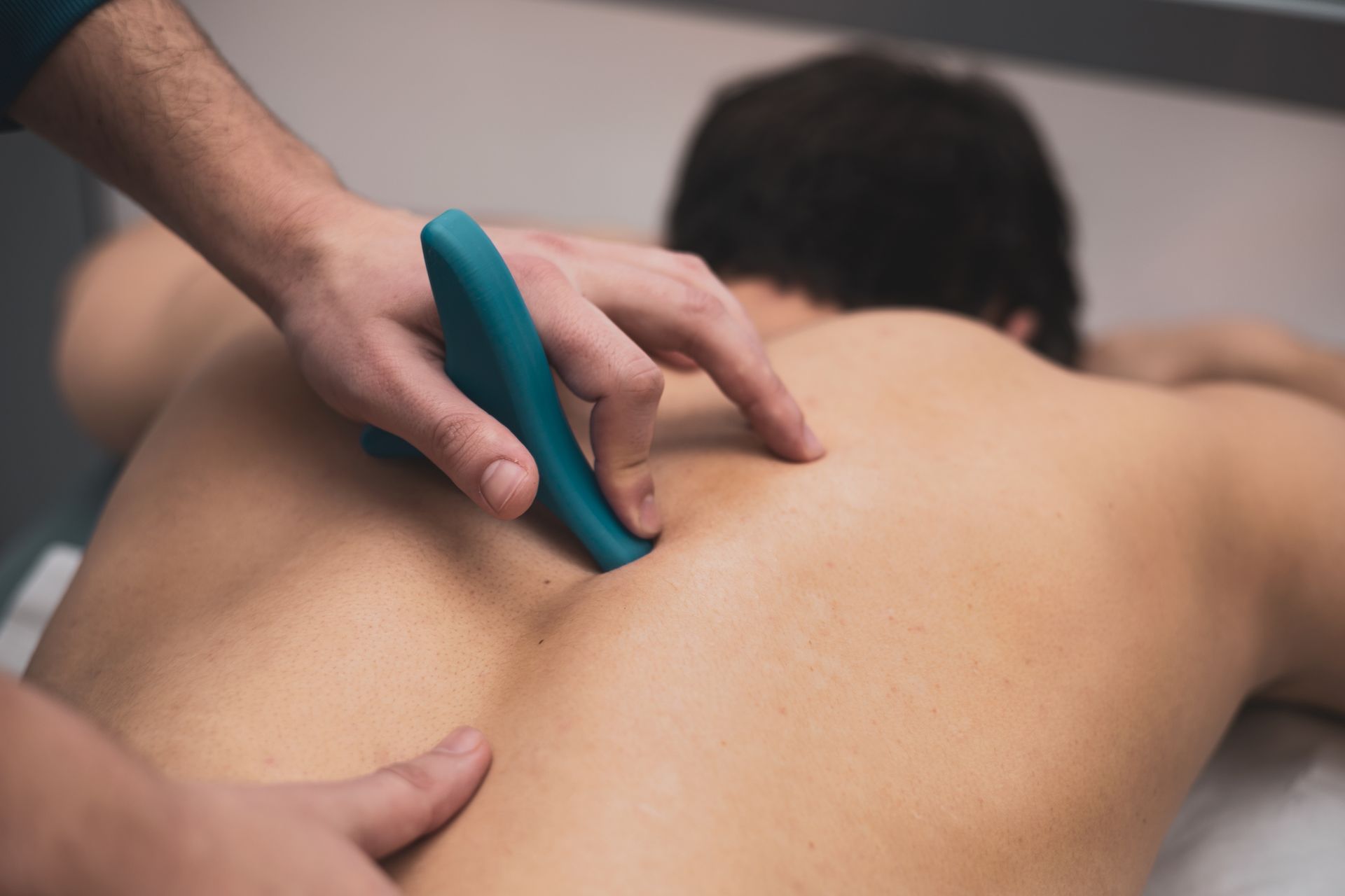 Massagetherapeutin verwendet während einer Behandlung ein türkisfarbenes Werkzeug auf dem nackten Rücken einer Person.