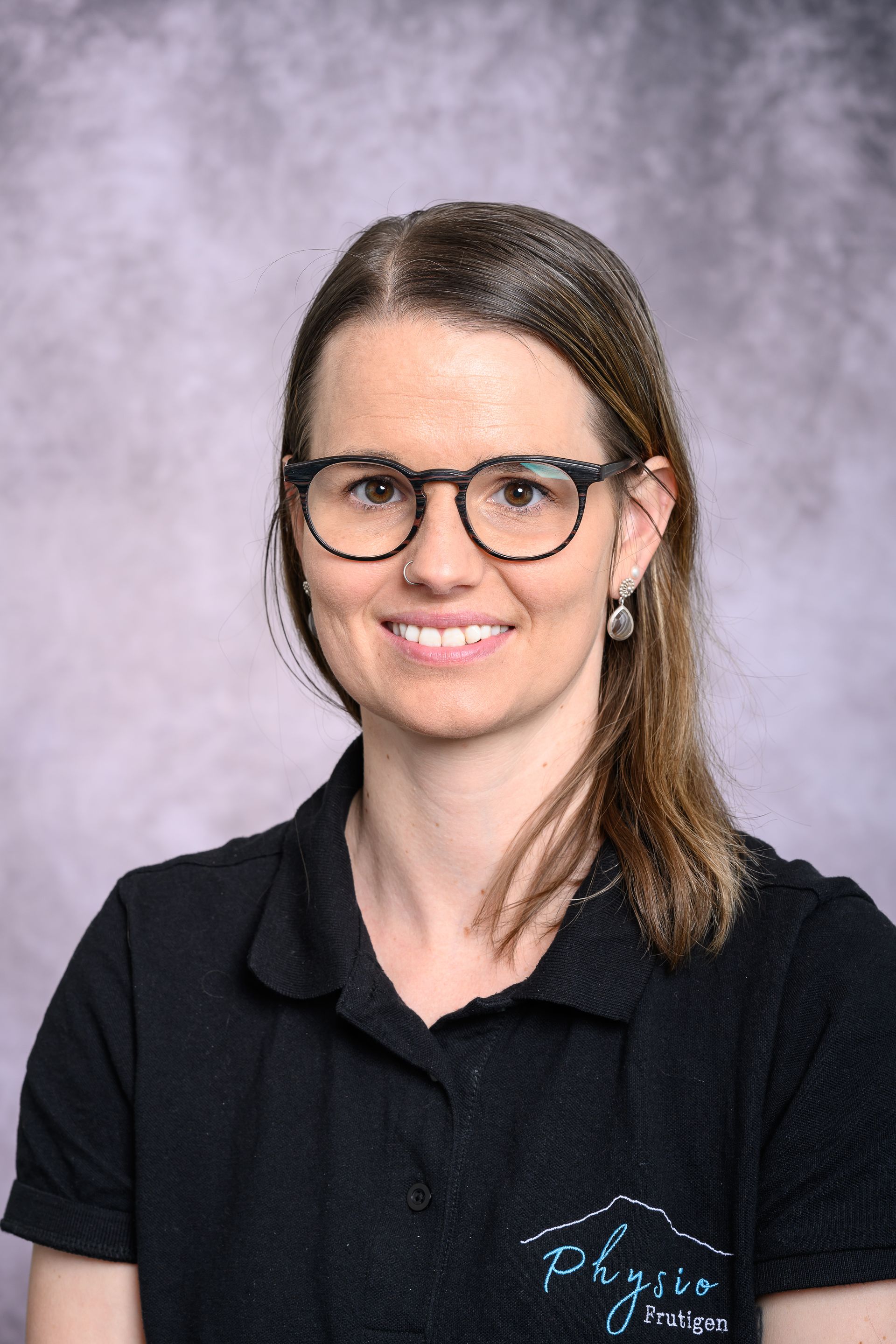 Porträt einer Person mit Brille und schwarzem Hemd vor grauem Studiohintergrund.