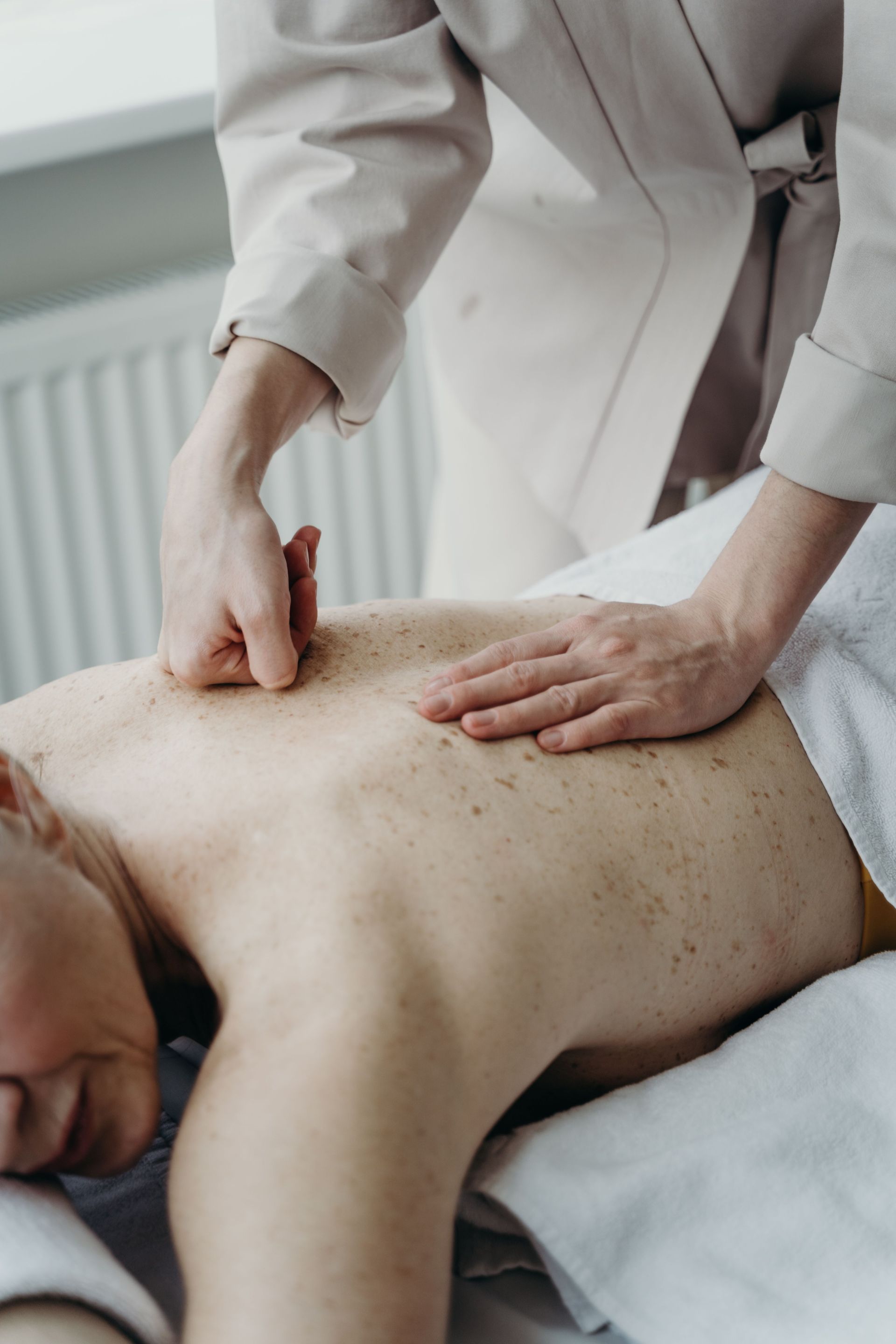 Ein Physiotherapeut dehnt in einer Klinik das Bein eines Patienten, während ein anderer Therapeut an einem Computer arbeitet.