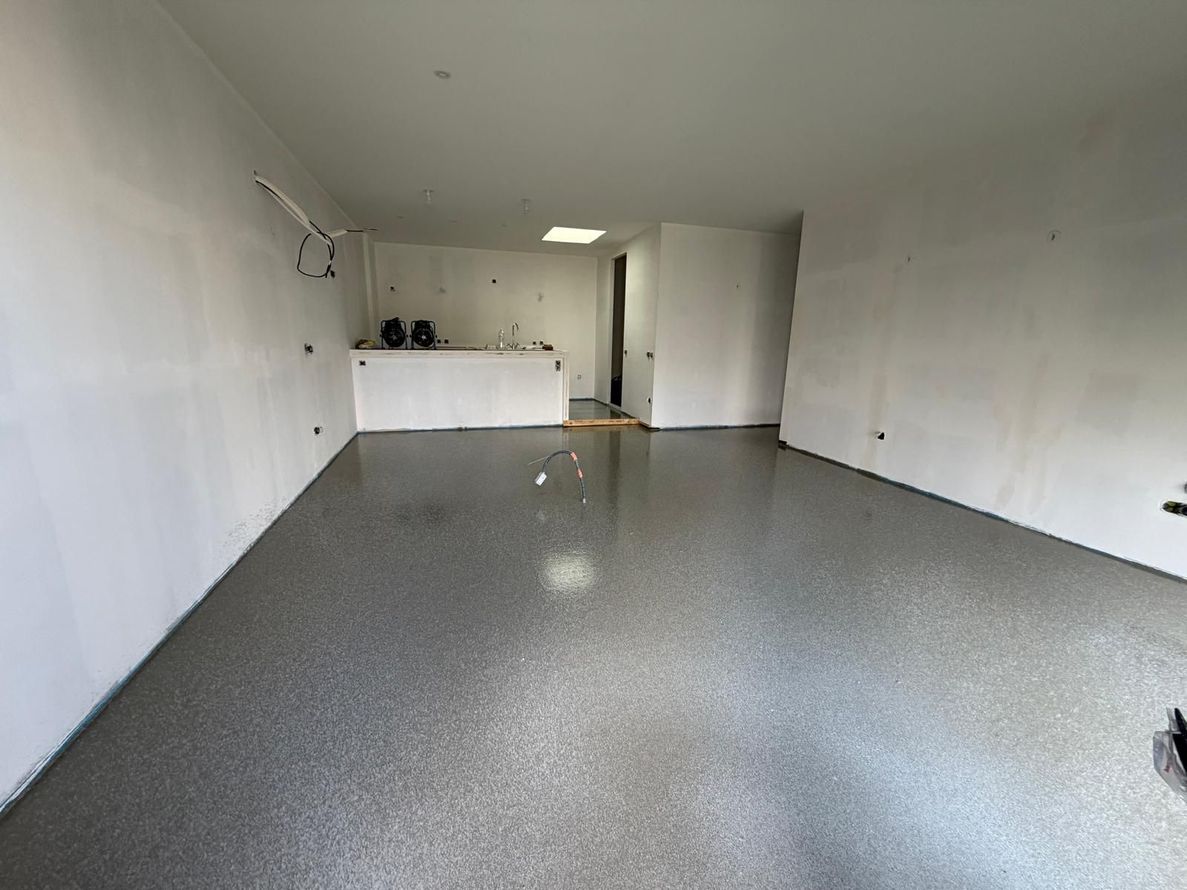 Garage blanc vide avec un sol gris moucheté et un petit comptoir au fond