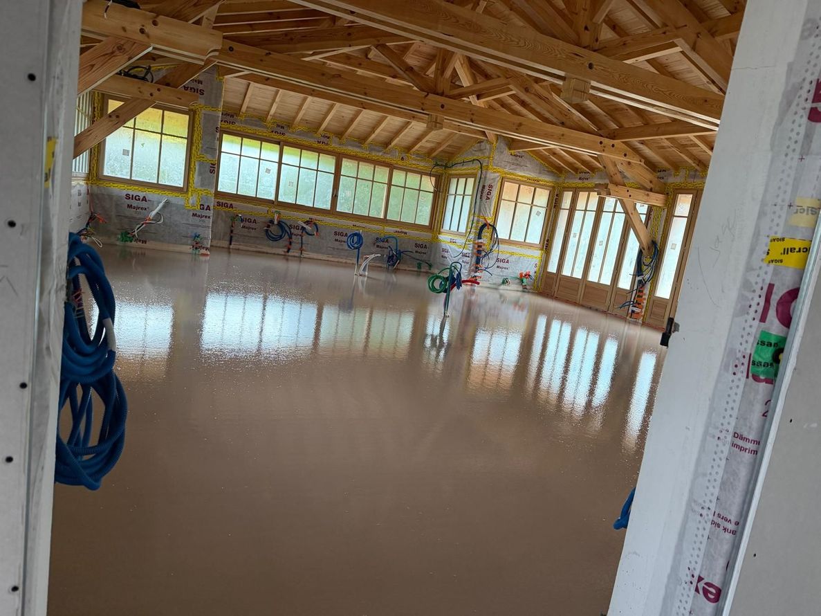 Intérieur en bois vide avec chape fluide et poutres apparentes, vu depuis une porte inachevée
