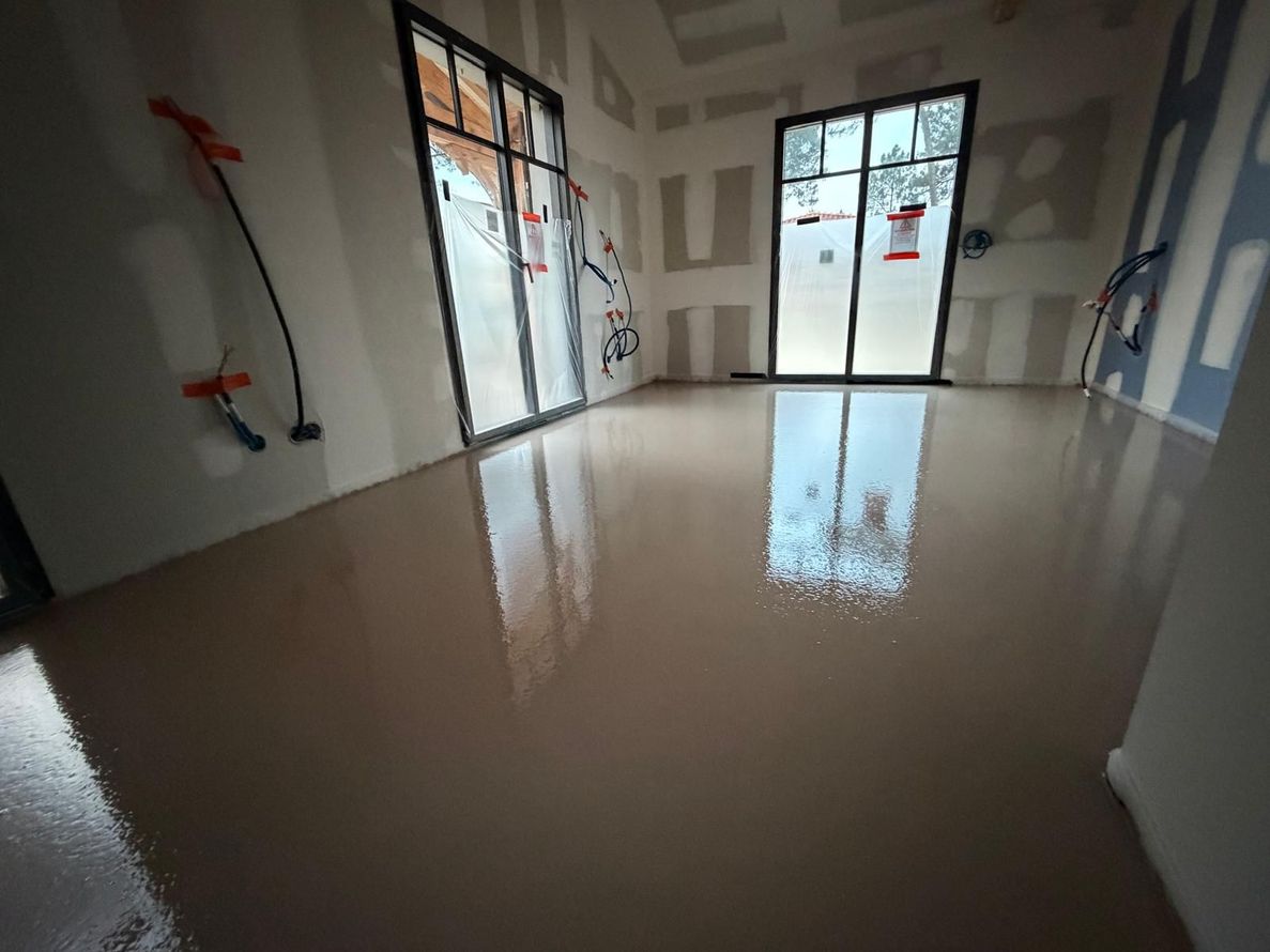 Pièce vide et inachevée avec sol brillant, cloisons sèches réparées et portes vitrées laissant entrer la lumière du jour