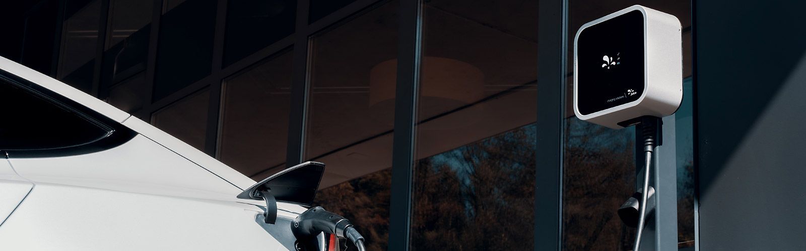 Weißes Elektroauto wird in der Nähe eines modernen Gebäudes aufgeladen.