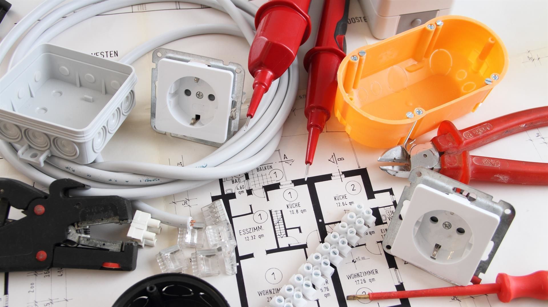 Elektrische Werkzeuge und Komponenten auf einem Bauplan, einschließlich Steckdosen, Kabel und Zangen.
