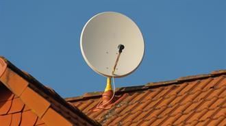 Satellitenschüssel auf einem roten Ziegeldach vor einem klaren blauen Himmel.