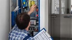 Elektriker überprüft Schalttafel, hält Klemmbrett in der Nähe des Aufzugs.