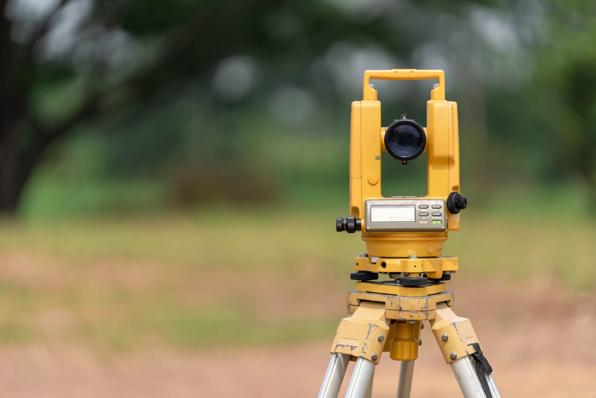 Un teodolito amarillo está sentado sobre un trípode en un campo.