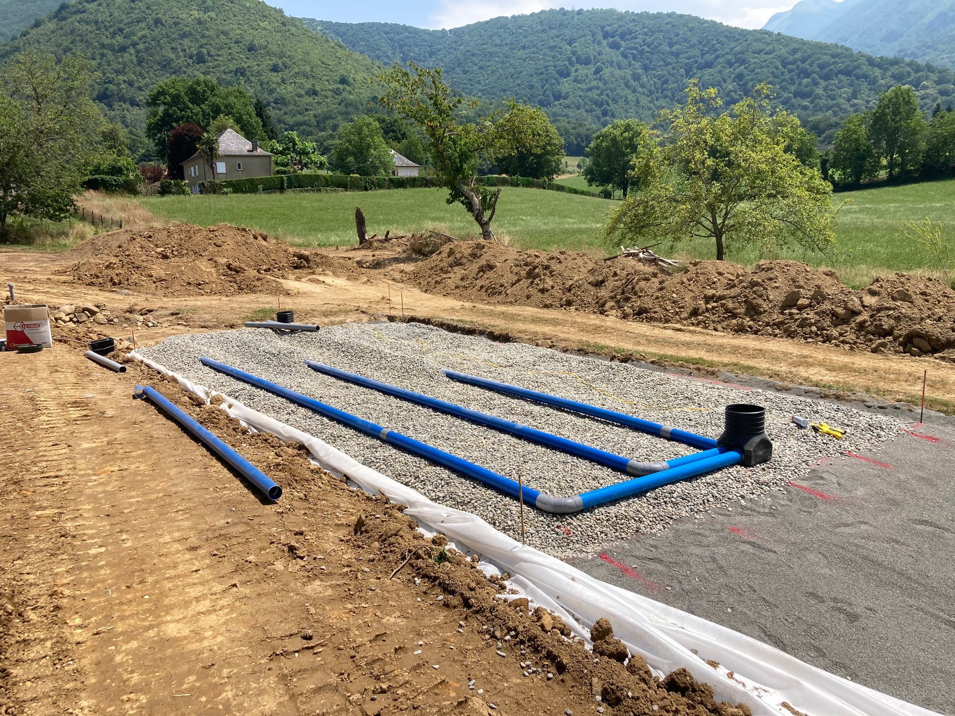 Chantier de construction avec des tuyaux bleus posés dans du gravier.