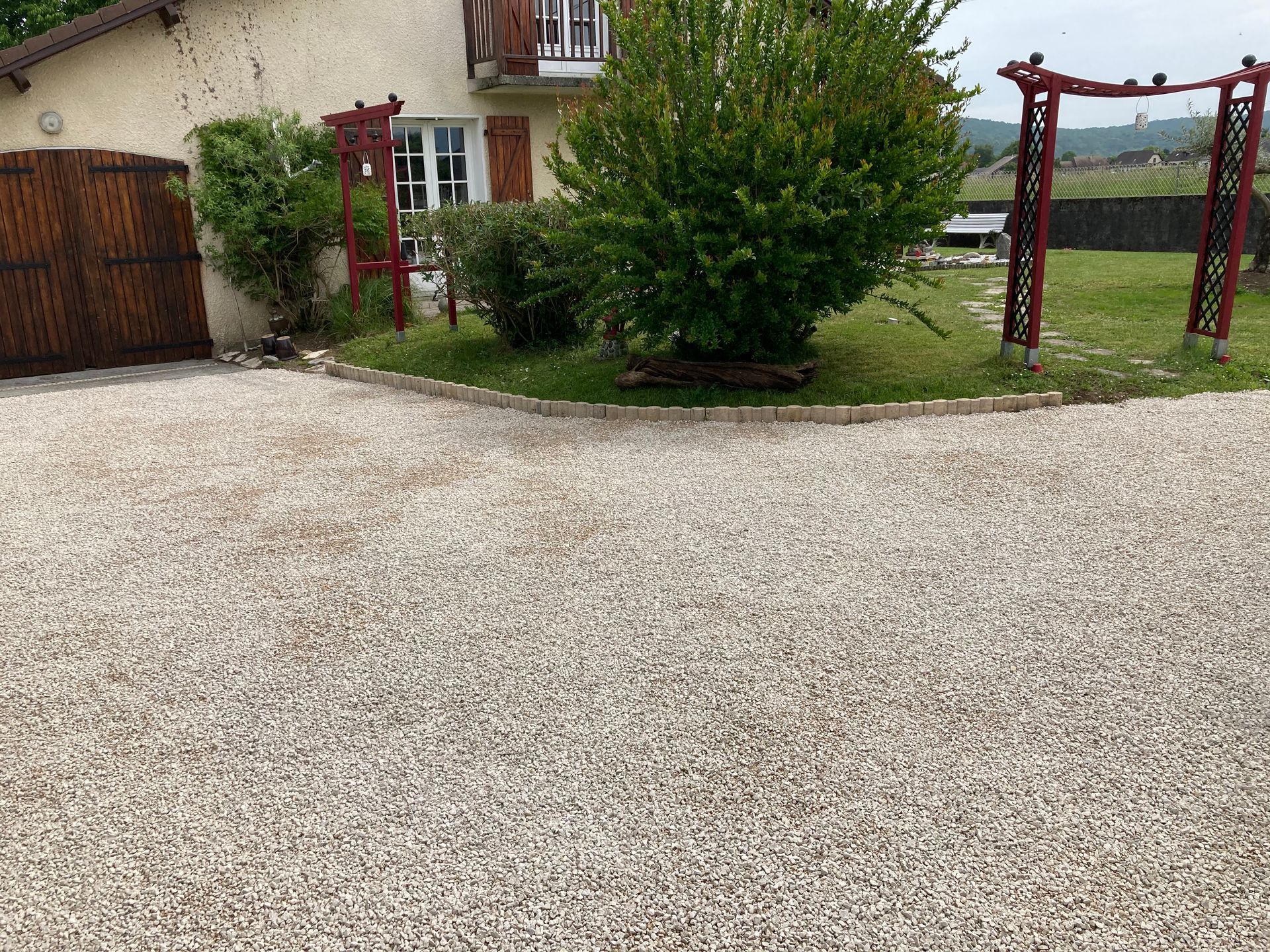 Allée de gravier menant à une maison de couleur claire avec un petit jardin devant la maison.