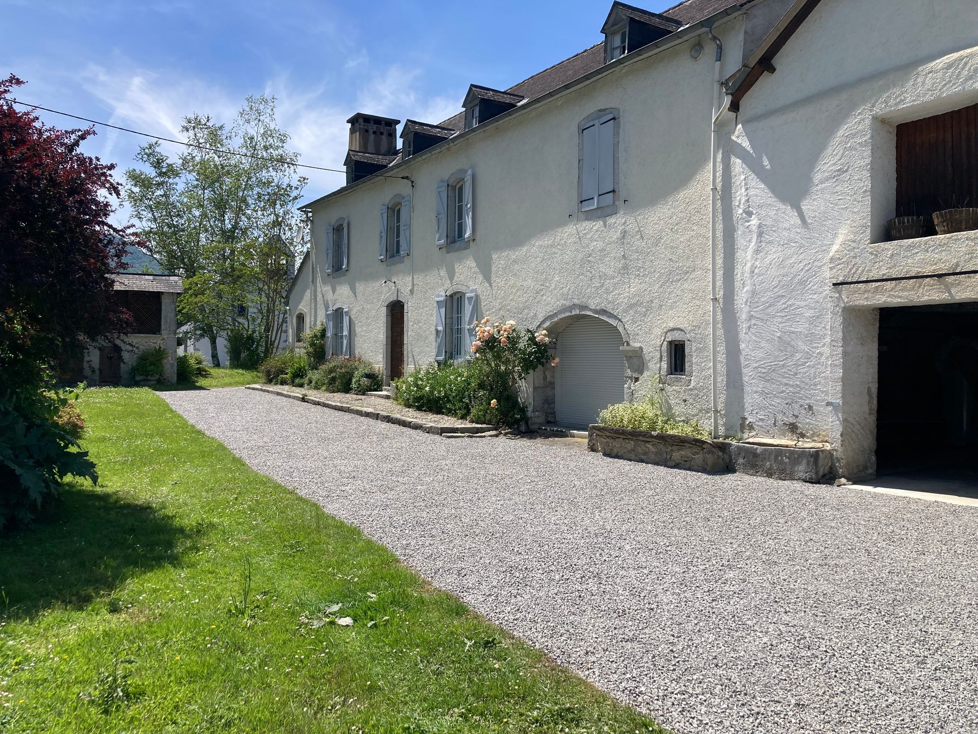 Bâtiment en pierre avec allée de gravier et pelouse verte. Volets bleus aux fenêtres.