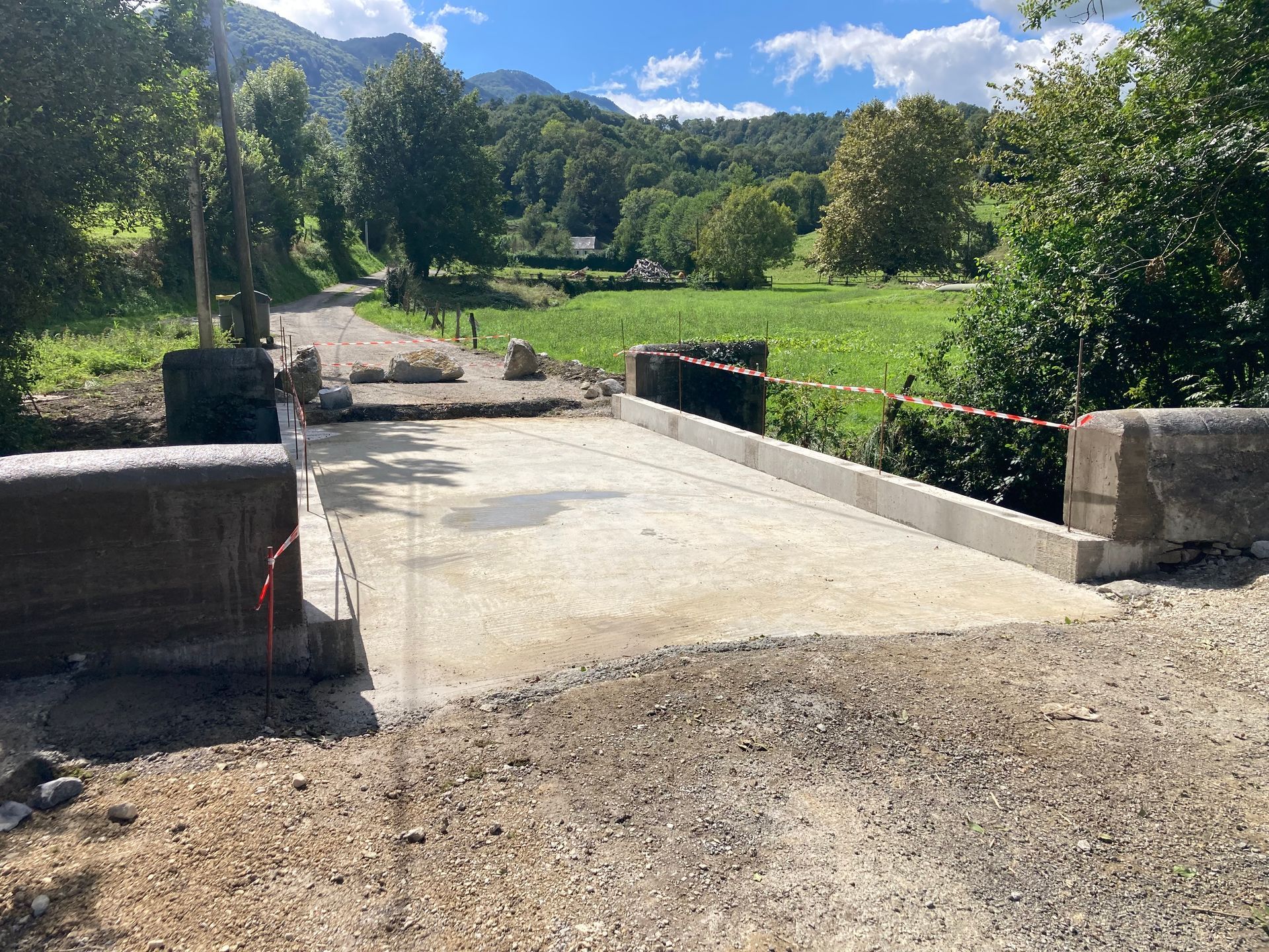 Nouveau pont en béton dans un cadre rural avec des montagnes et des arbres en arrière-plan.