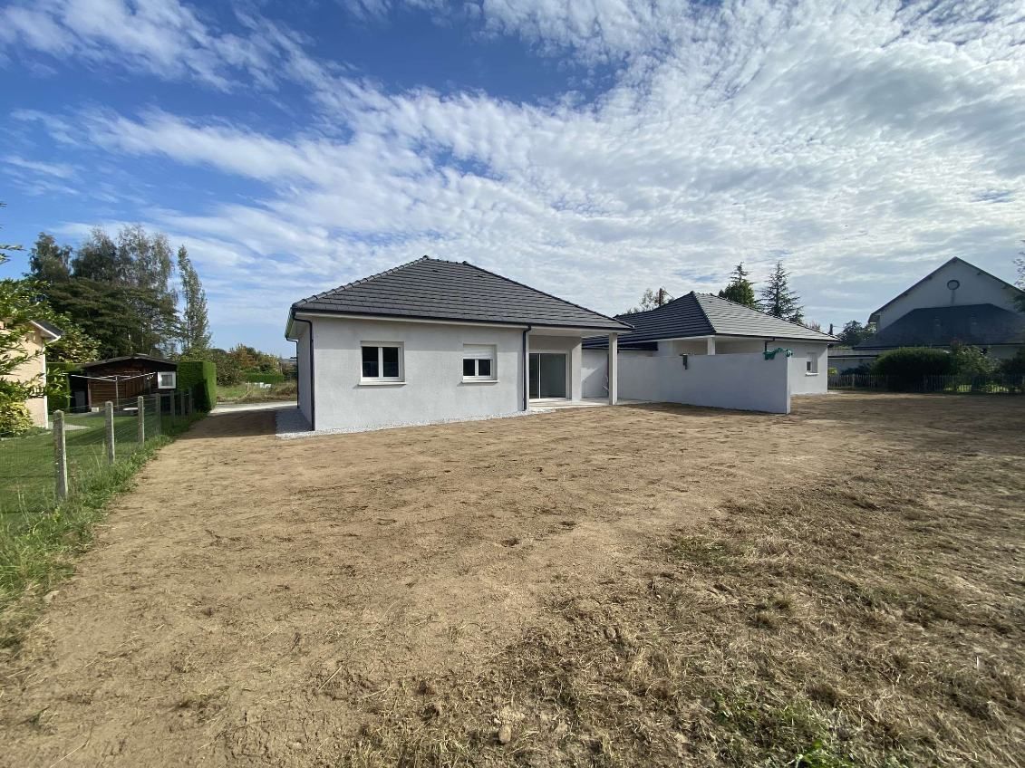 Vue extérieure d'une maison nouvellement construite avec un jardin brun sous un ciel partiellement nuageux.