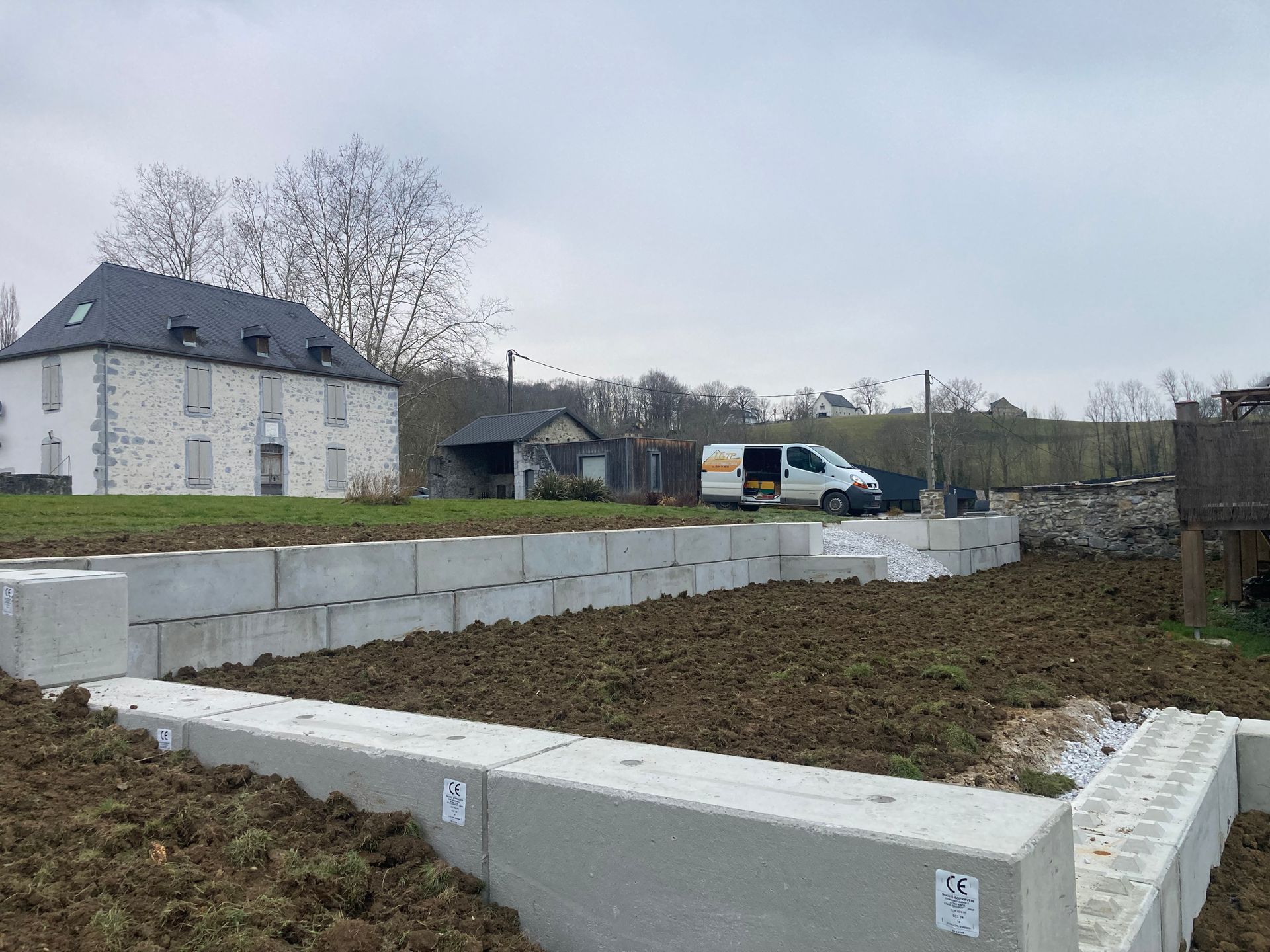 Chantier de construction avec des blocs de béton au premier plan, de la terre et une camionnette blanche.
