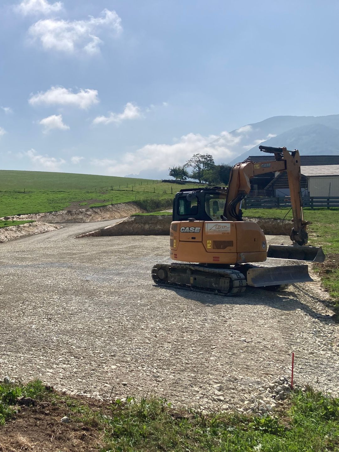 Une excavatrice sur un chemin de gravier dans un champ sous un ciel nuageux.