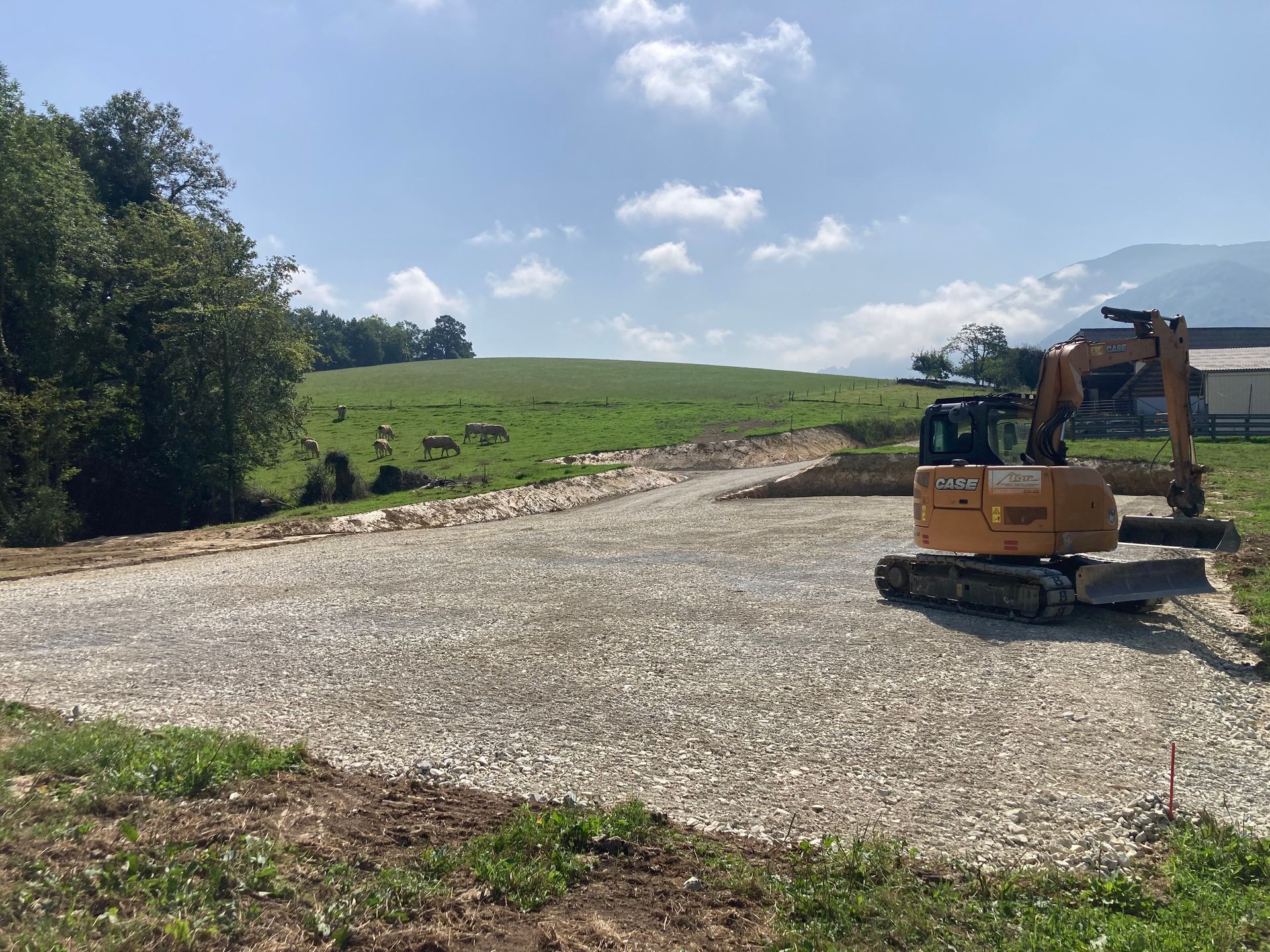 Chantier de construction avec sol gravillonné et excavatrice ; colline verdoyante en arrière-plan.