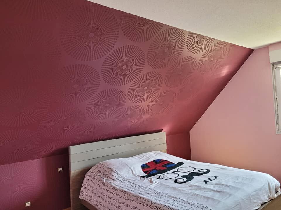 Chambre avec un lit, une tête de lit blanche, des murs roses et un mur d'accent à motifs inclinés.