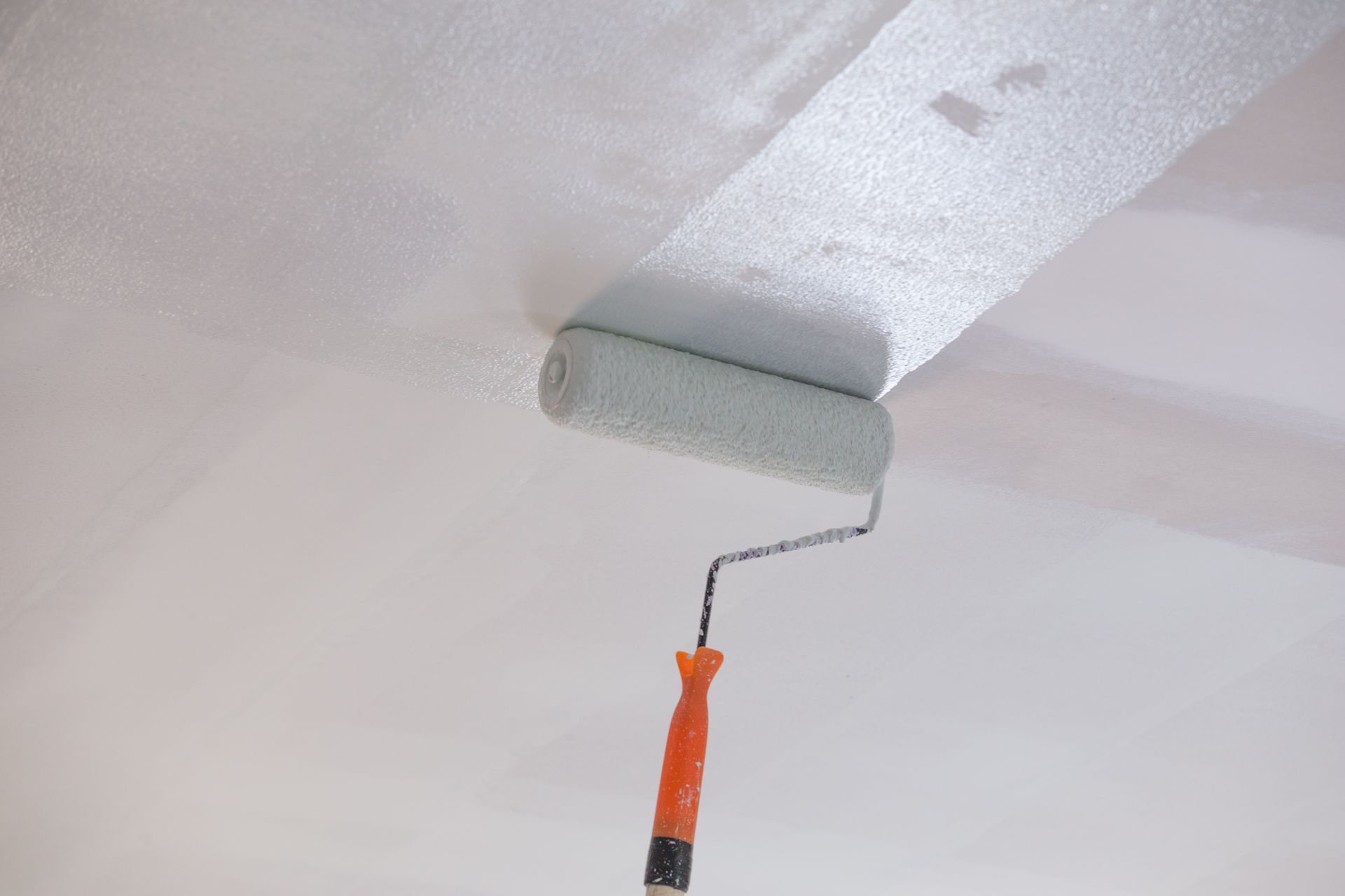 Rouleau à peinture appliquant de la peinture gris clair sur un joint de plafond blanc
