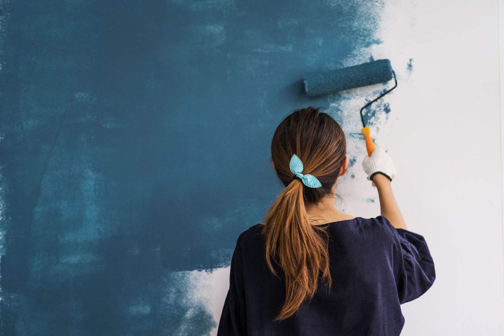 Une personne peint un mur en bleu au rouleau dans une pièce en rénovation