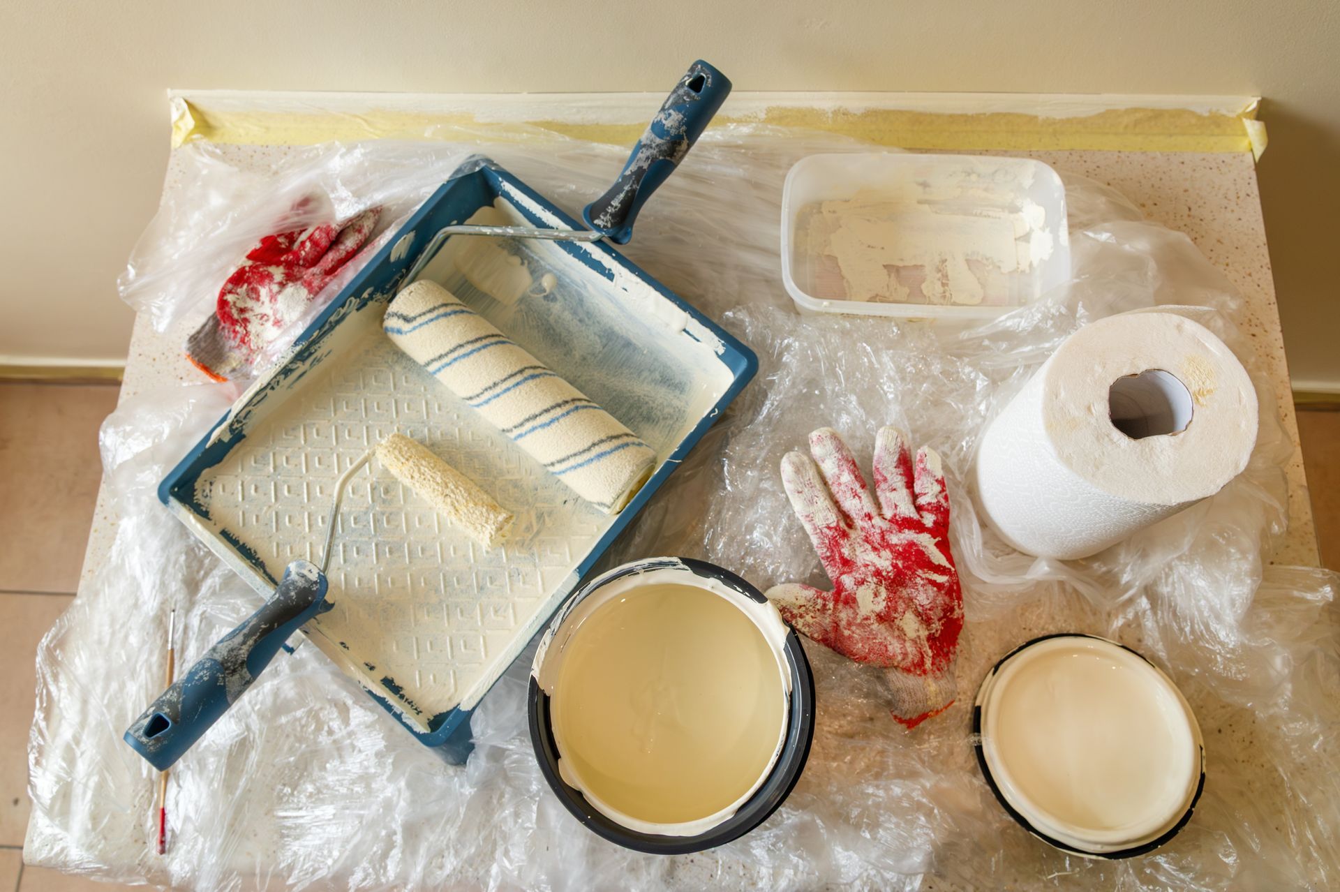 Bac à peinture et rouleaux avec de la peinture blanche sur une surface de travail recouverte de plastique