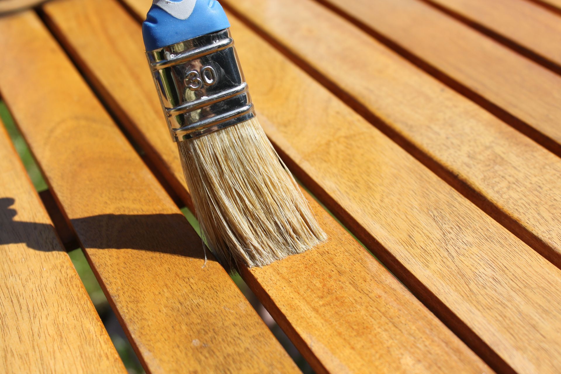 Un pinceau applique du vernis sur une terrasse en bois au soleil.