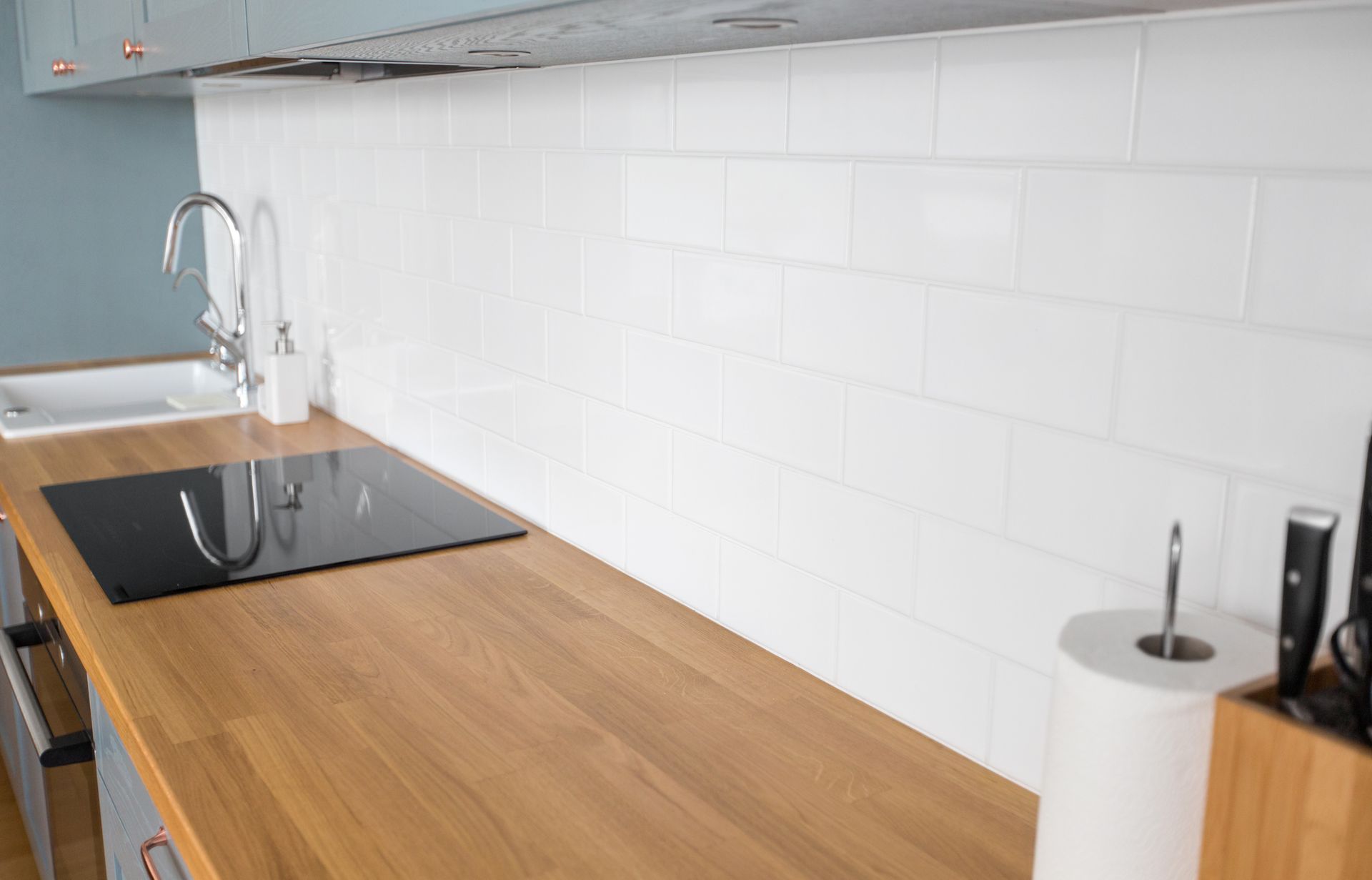 Cuisine moderne avec comptoir en bois, plaque de cuisson noire, crédence en carrelage blanc et robinet d'évier