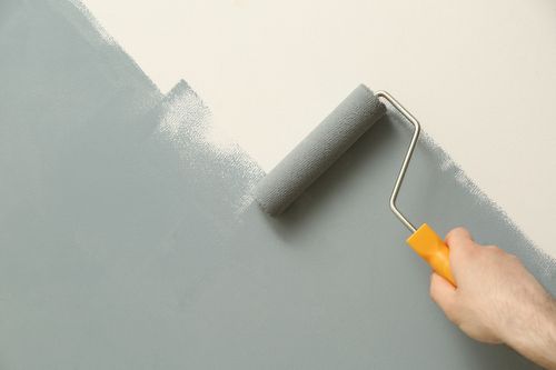 Une main peint un mur gris au rouleau, créant un bord en diagonale.