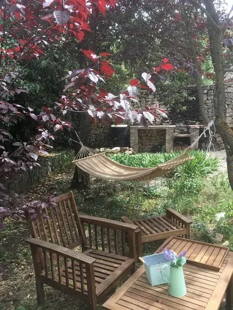 Una mesa y sillas de madera en un jardín con una hamaca al fondo.