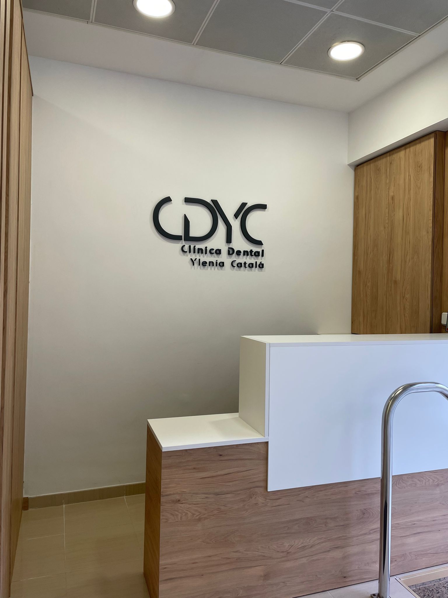 Zona de recepción con pared azul, mostrador de madera, nombre “Dra. Vlenia Catala” y una pequeña planta.