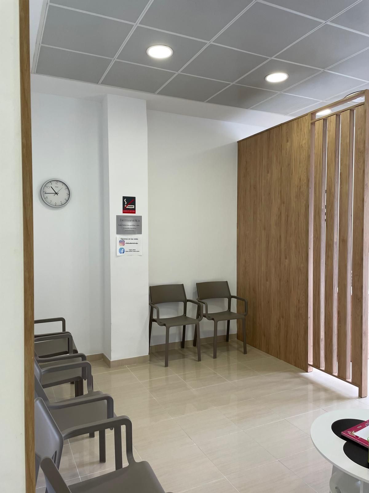 Sala de espera con sillas azules, una mesa pequeña con folletos y una mesa para niños. Paredes blancas y azules.