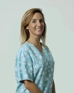 Una mujer con una blusa médica azul claro con estampado floral sonríe y mira hacia la derecha.