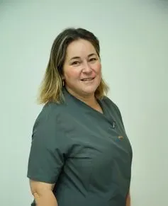 Una mujer con uniforme verde sonríe a la cámara en una habitación blanca.