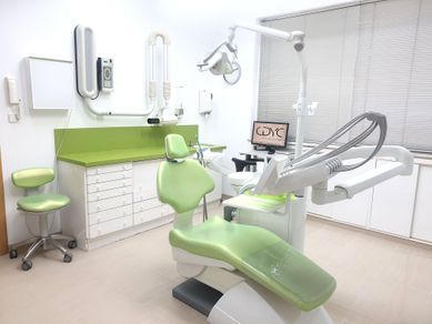 Consultorio dental con silla y armarios verdes. Equipo médico, ambiente luminoso y limpio.