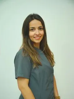Mujer de cabello castaño largo, con una bata verde azulada, sonriendo. Fondo blanco.