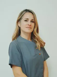 Mujer con cabello rubio con una blusa médica azul, mirando a la cámara.