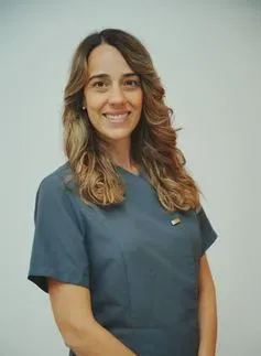 Mujer sonriente con uniforme azul, posiblemente trabajadora de la salud.
