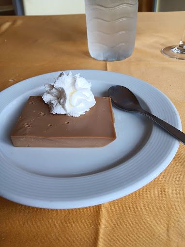 Un plato blanco cubierto con un trozo de postre de chocolate con crema batida y una cuchara.