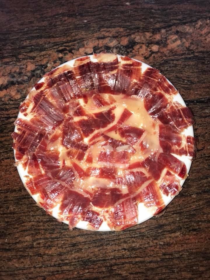 Un plato blanco cubierto con carne y queso sobre una mesa de madera.