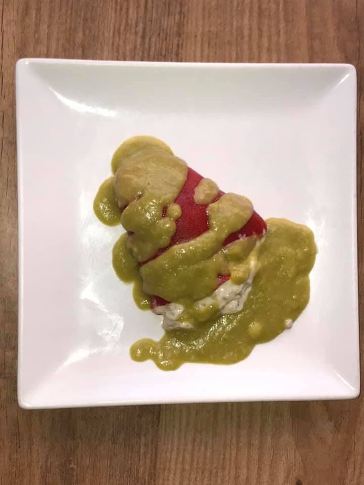 Un plato blanco cubierto con un trozo de comida y salsa sobre una mesa de madera.