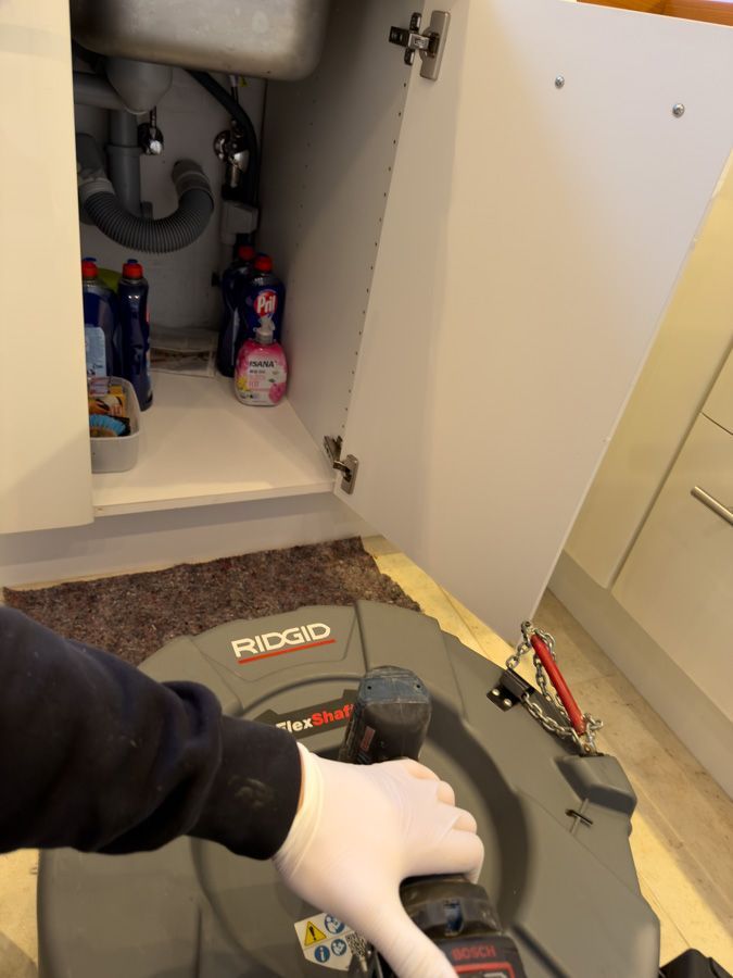 Eine behandschuhte Hand hält eine RIDGID-Abflussspirale neben einem offenen Badezimmerschrank unter einem Waschbecken.