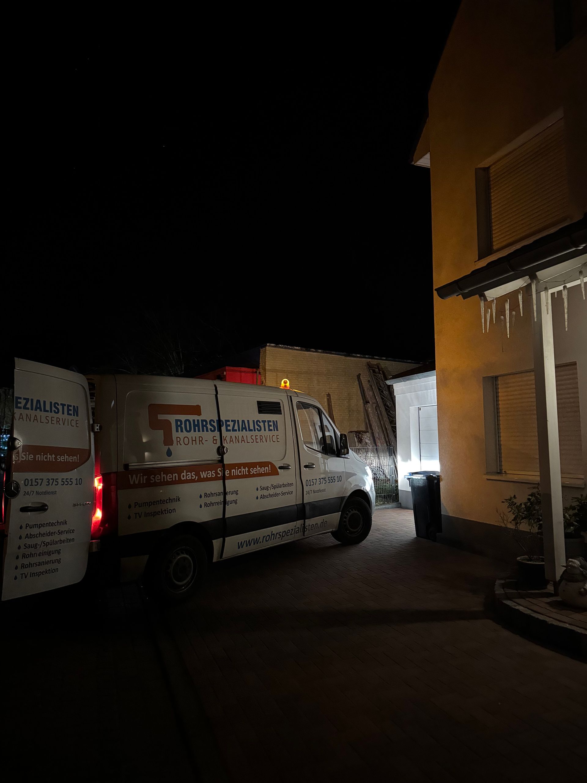Eine Straße bei Nacht mit weißen Lieferwagen, die neben einem beleuchteten Gebäude parken, und einem dunklen Himmel.