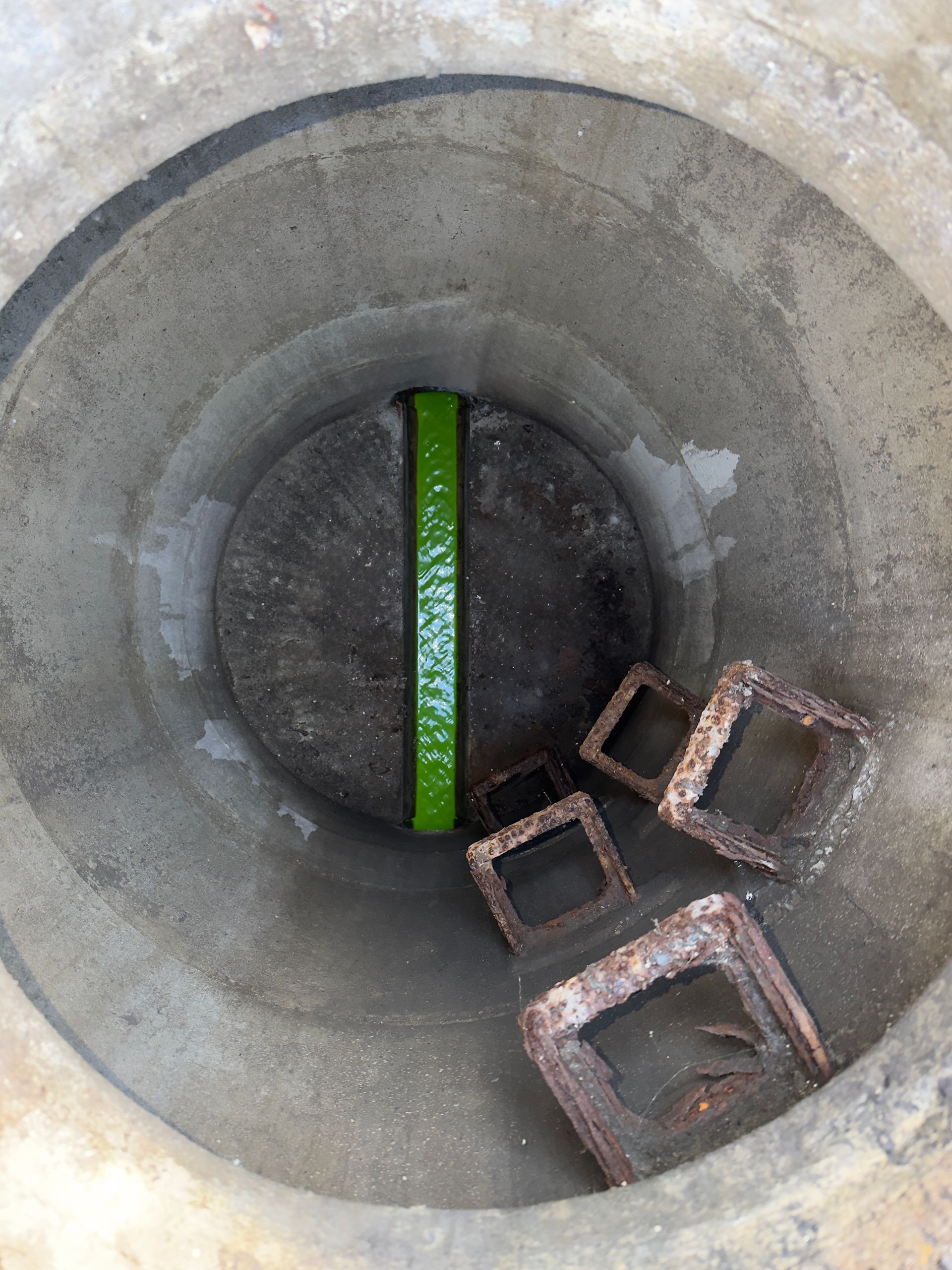 Betonrohr-Innenraum mit einer grünen Nivellierlatte und mehreren rostigen Metallblöcken unten rechts