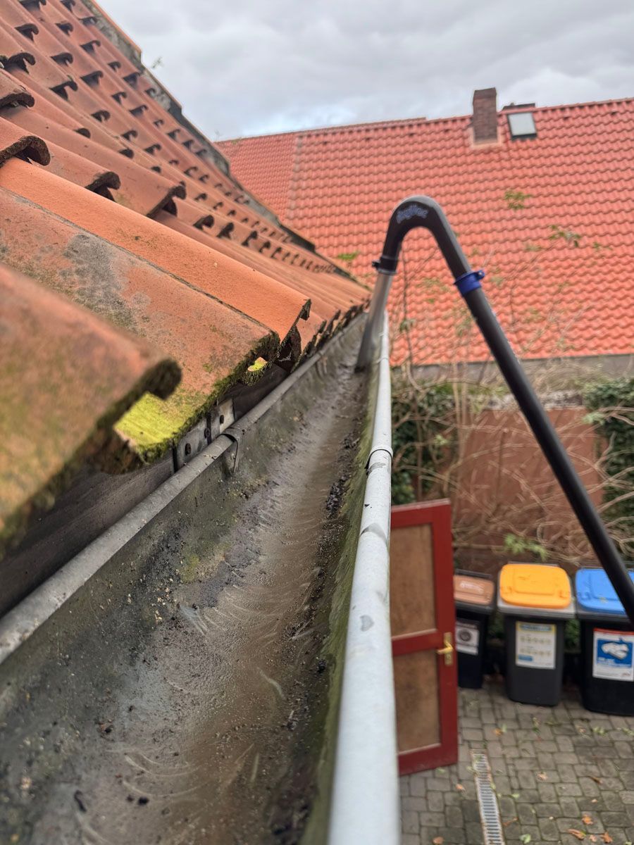 Eine Dachrinne mit einem daran befestigten Schlauch und ein Dach im Hintergrund.