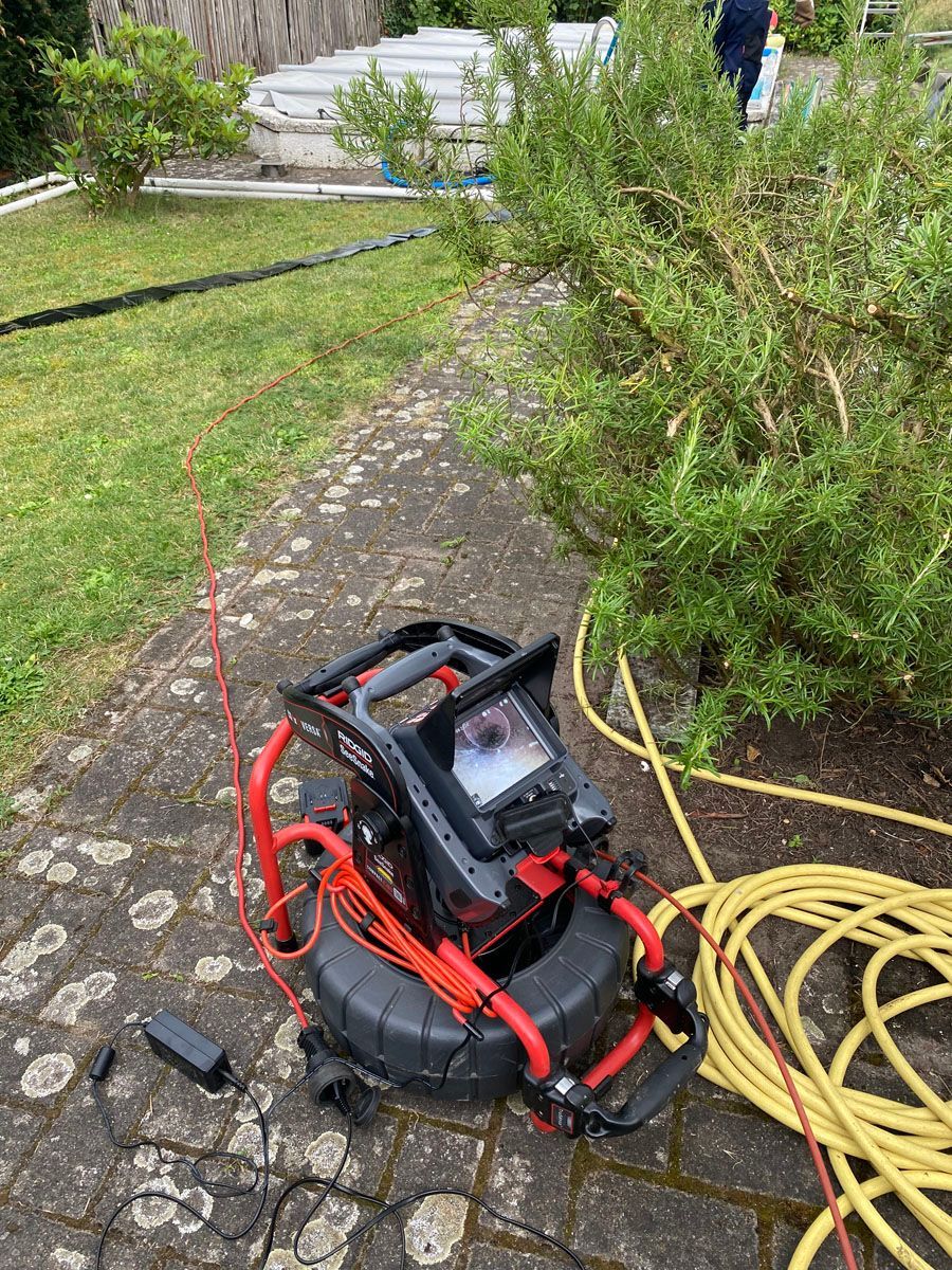 Eine Abflusskamera steht auf einem Gehweg neben einem Schlauch.