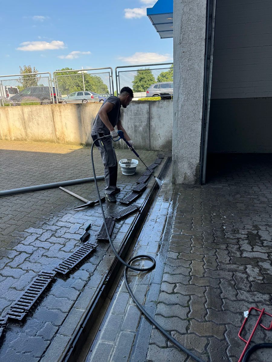 Ein Mann reinigt einen Gehweg aus Ziegeln mit einem Schlauch.