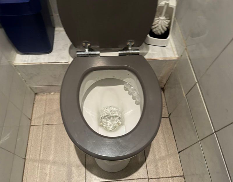 Eine Toilette steht in einem Badezimmer neben einem Mülleimer und einer Toilettenbürste