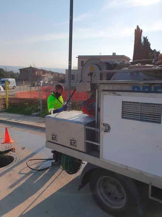 Un trabajador vestido de verde neón opera un equipo desde un camión blanco cerca de un pozo abierto en una calle de la ciudad.