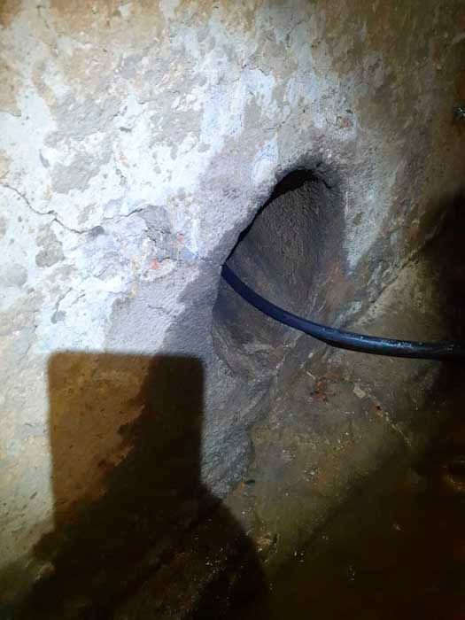 Un agujero oscuro y áspero en una pared; un cable negro pasa a través de él.